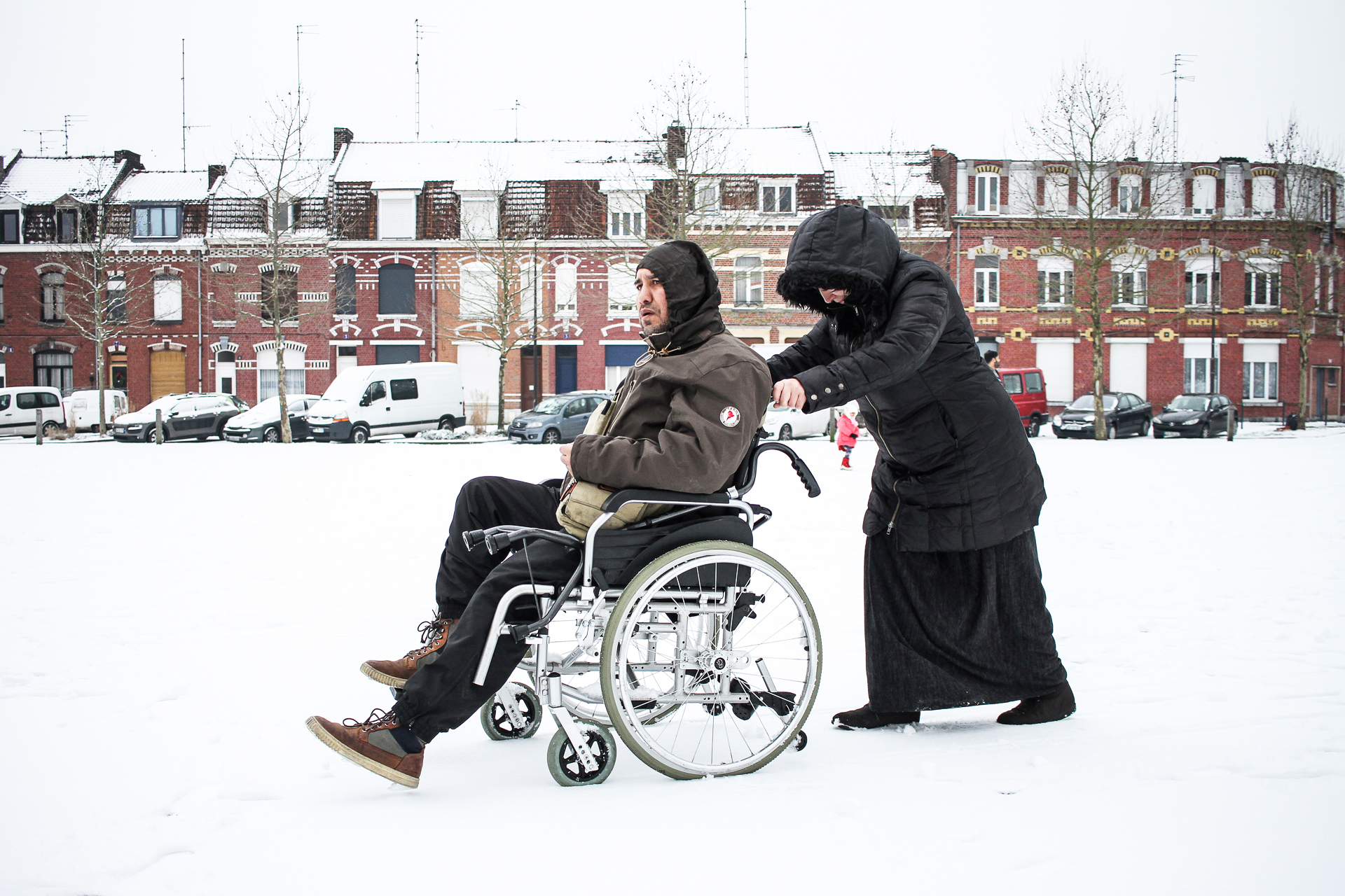 Image d'une femme poussant le fauteuil roulant de son mari dans la neige à Roubaix par Anouk Desury