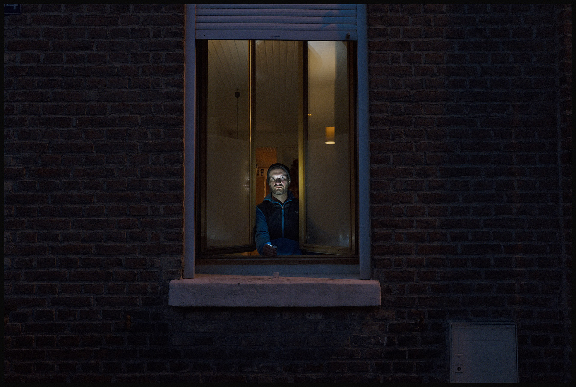 Durant la période de confinement, image d'un homme dans la nuit à la fenêtre de sa maison par Ludovic Leleu