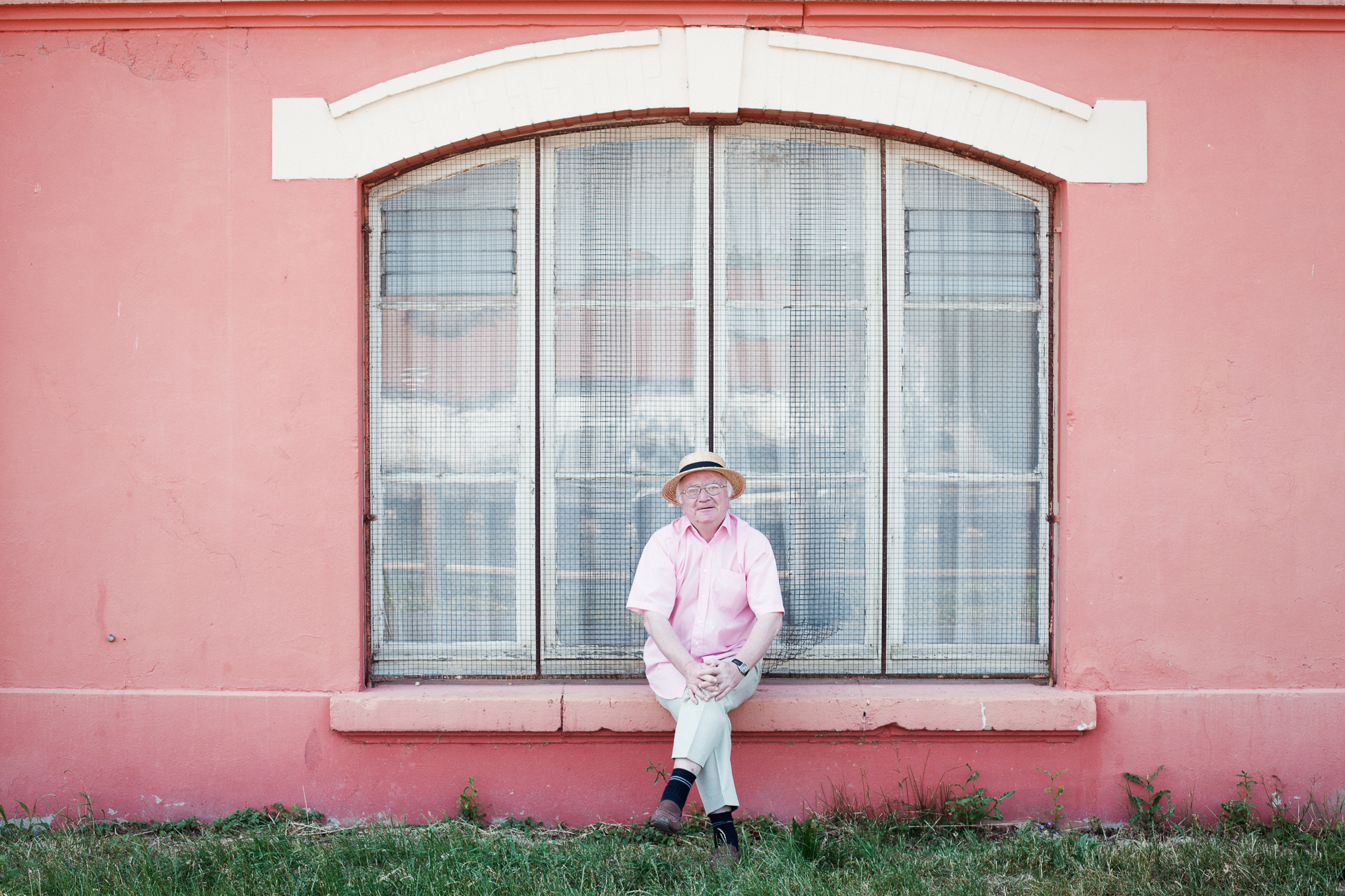 Photographie d'un habitant assis devant sa maison au style architecturale rose par Bertrand Jamot