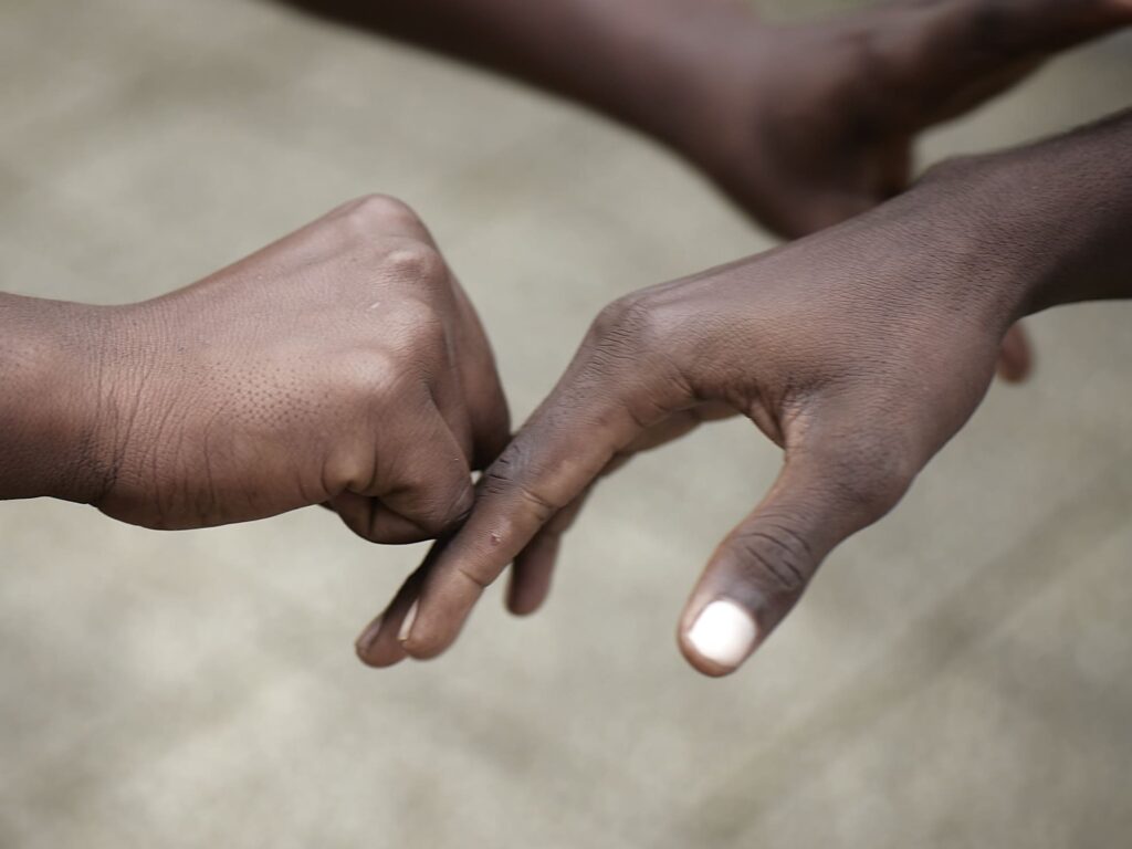 Photographie de Zélie Hallosserie / Light Motiv, issue de la série intitulée The Game, représentant un gros plan de deux mains d'enfants dans un geste complice, dans le cadre d'un reportage documentaire porté sur le voyage des migrants dans le nord de la France, sur la côte.