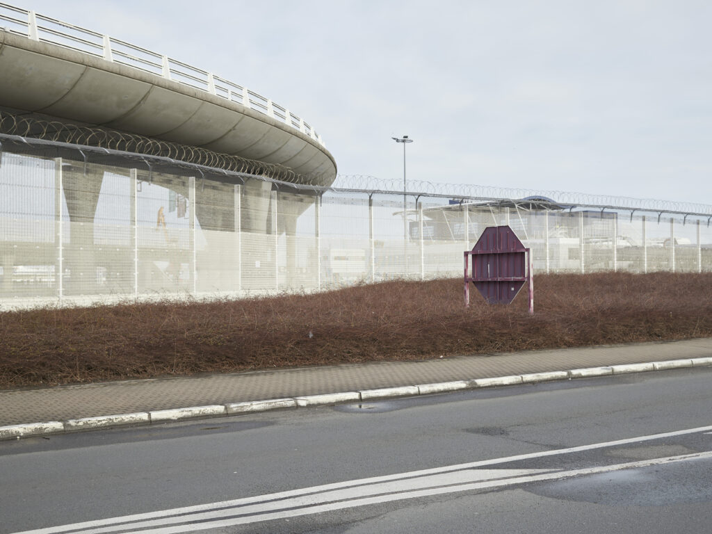 Photographie de Zélie Hallosserie / Light Motiv, issue de la série intitulée The Game, représentant un homme assis dans un intérieur au t-shirt blanc qui regarde à côté de la caméra d'un air perdu, dans le cadre d'un reportage documentaire porté sur le voyage des migrants dans le nord de la France, sur la côte.