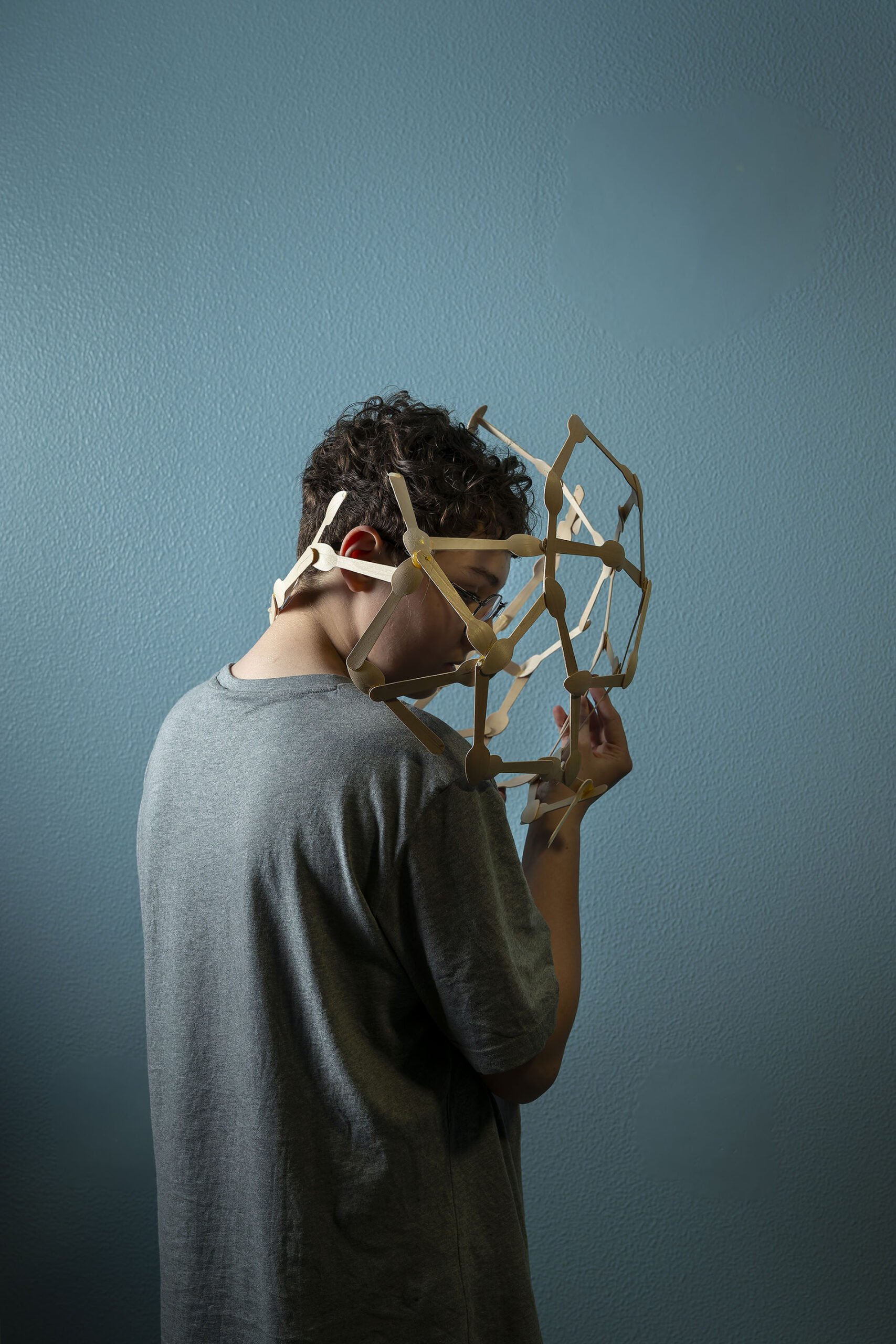 Photographie de Lionel Pralus issue de sa série intitulée "dés-équilibres" représentant une personne aux cheveux courts et bouclés tenant une structure en bois ajourée lui entourant la tête.