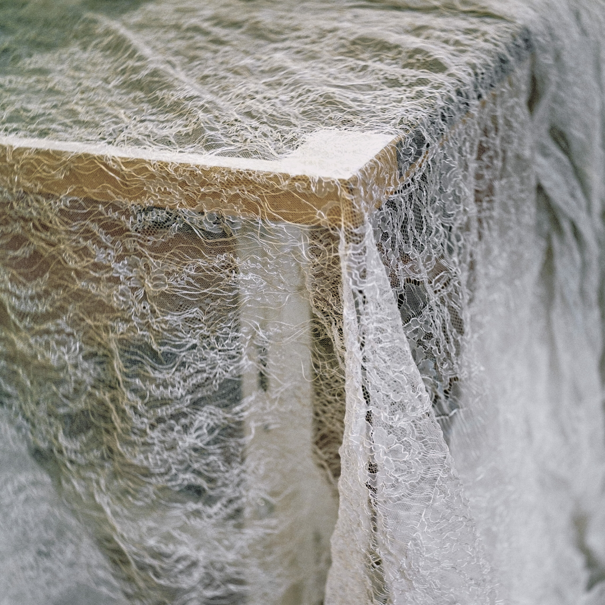 Photographie de Zélie Hallosserie / Light Motiv, issue de la série intitulée Dentelle Calais Caudry, représentant un grand tissu de dentelle blanche posé sur le coin d'une table en bois brun, dans le cadre d'un reportage qui témoigne du travail et de la conception de la dentelle à Calais.