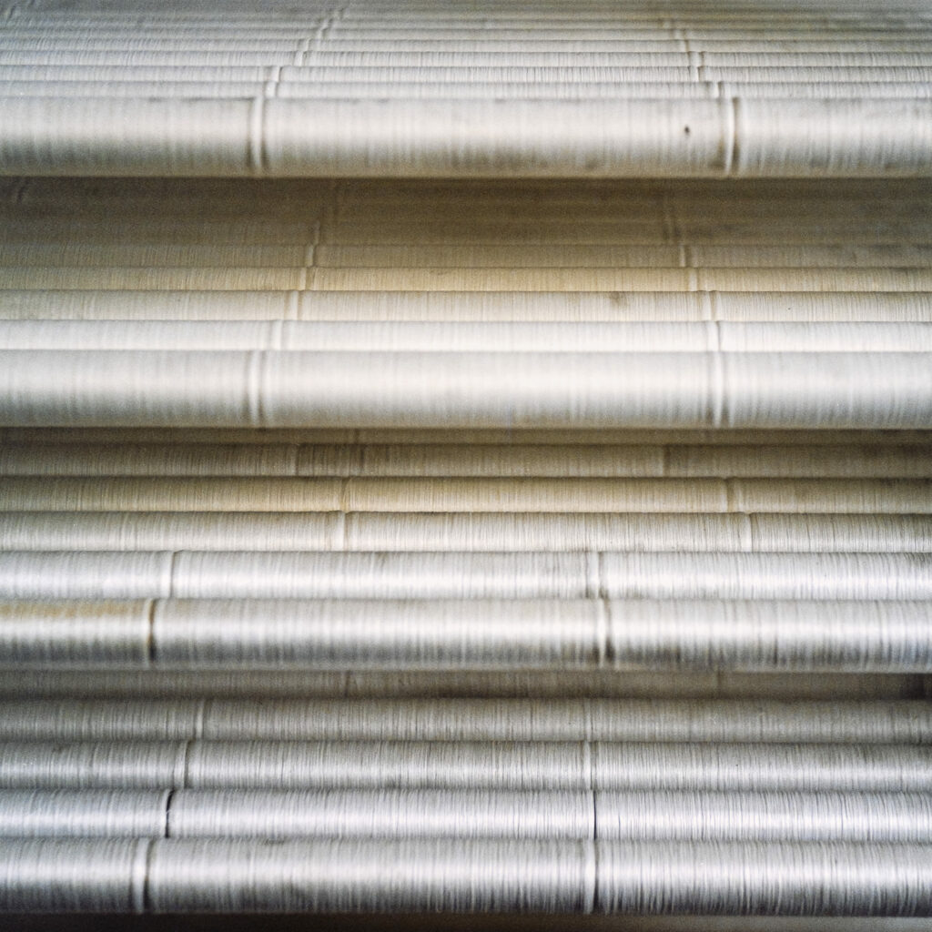 Photographie de Zélie Hallosserie / Light Motiv, issue de la série intitulée Dentelle Calais Caudry, représentant une collection de bobines de fils blanc disposés les uns sur les autres à la manière d'une étagère, dans le cadre d'un reportage qui témoigne du travail et de la conception de la dentelle à Calais.