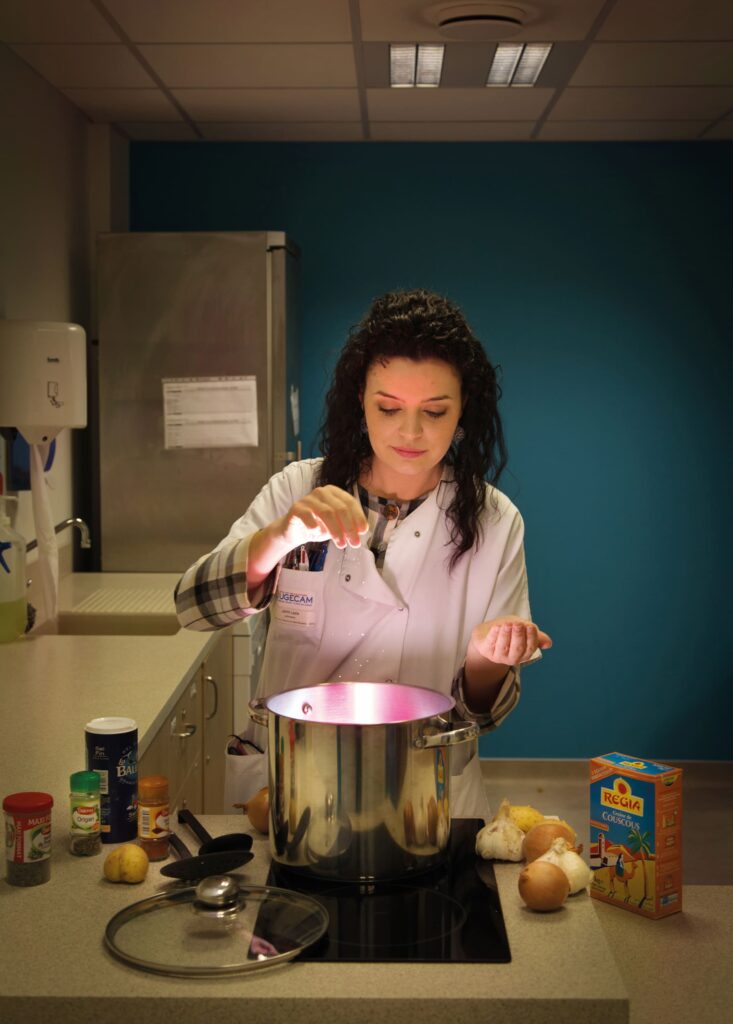 Photographie de Lionel Pralus / Light Motiv, issue de la série intitulée Désordre Ordinaire datant de 2020, représentant une jeune femme au dessus d'une marmite sur une plaque de cuisson dont jaillit une lumière rosée, dans le cadre d'un projet tourné autour de mise en scène photographiques avec les patients et professionnels du SAAS.