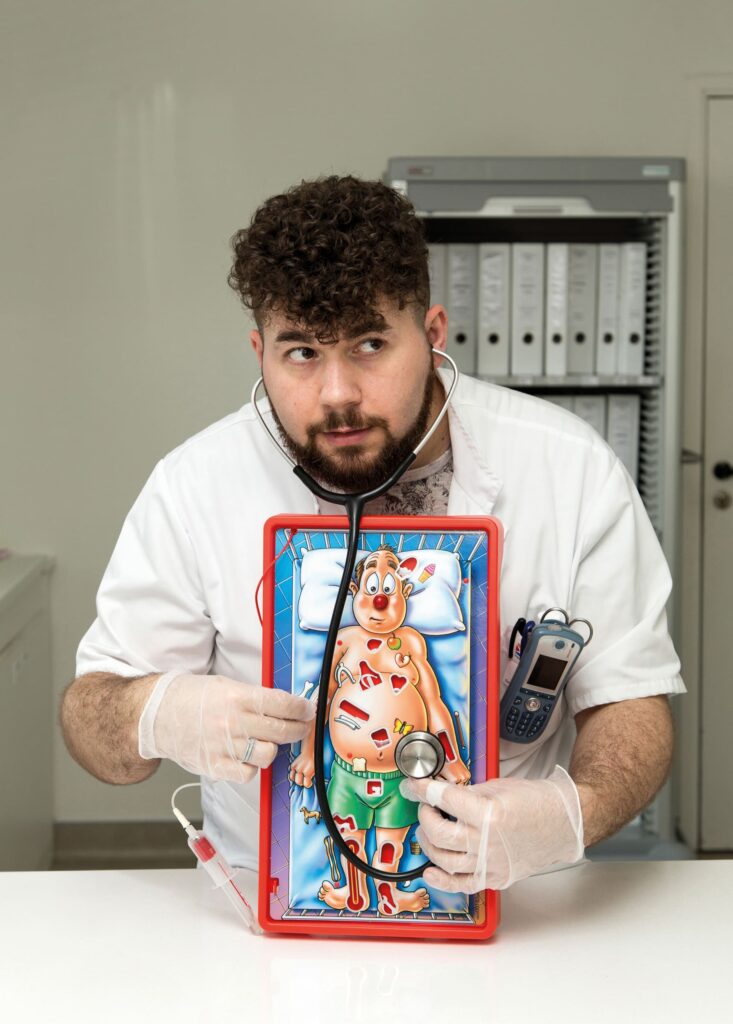 Photographie de Lionel Pralus / Light Motiv, issue de la série intitulée Désordre Ordinaire datant de 2020, représentant un homme en blouse blanche jouant au jeu de Docteur Maboul, dans le cadre d'un projet tourné autour de mise en scène photographiques avec les patients et professionnels du SAAS.