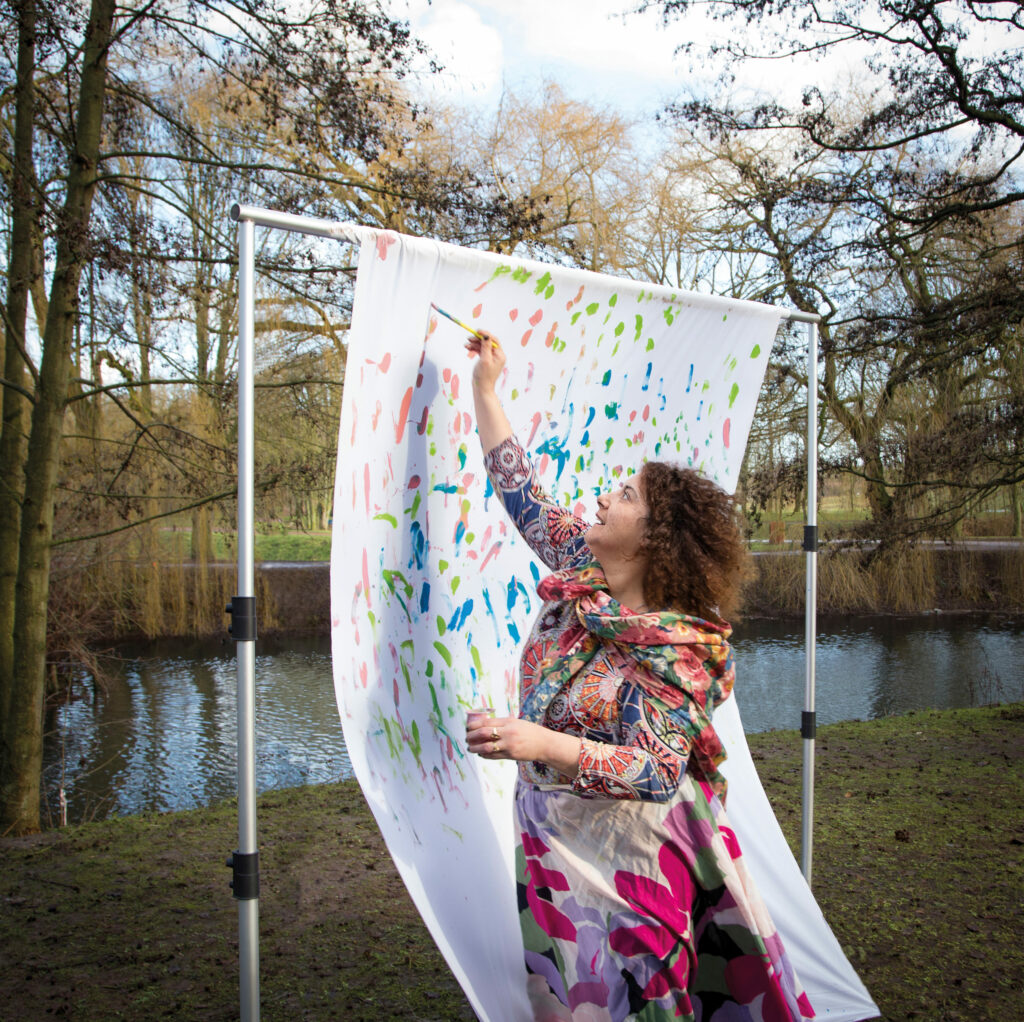 Photographie de Lionel Pralus / Light Motiv, issue de la série intitulée Désordre Ordinaire datant de 2020, représentant une femme peignant en extérieur sur un long tissu blanc accroché à un portant, dans le cadre d'un projet tourné autour de mise en scène photographiques avec les patients et professionnels du SAAS.