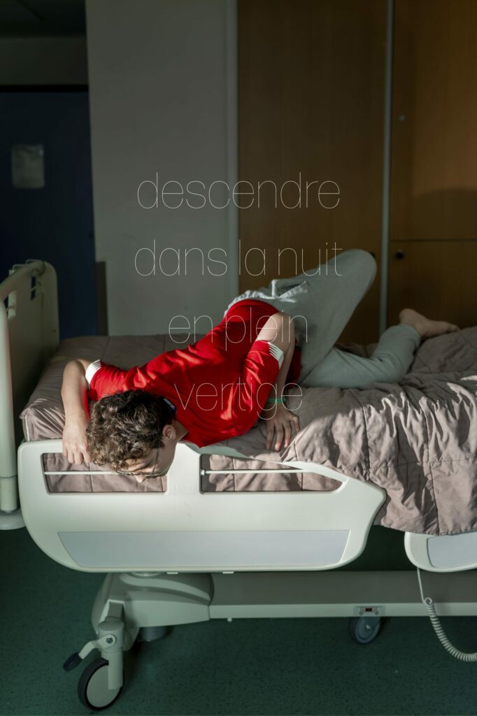 LP - LE JOUR LA NUIT Photographie de Lionel Pralus / Light Motiv, issue de la série intitulée Le Jour La Nuit datant de 2024, représentant un jeune homme étendu sur un lit d'hôpital la tête tournée vers le sol avec un texte en filigrane "descendre dans la nuit en plein vertige", dans le cadre d'un projet tourné autour de jeunes et de l'éclairage hospitalier.