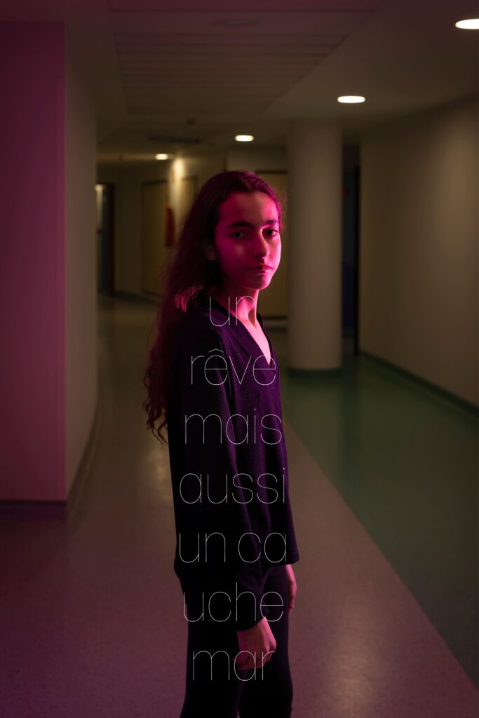 Photographie de Lionel Pralus / Light Motiv, issue de la série intitulée Le Jour La Nuit datant de 2024, représentant une jeune fille le visage tourné vers l'objectif debout dans un couloir d'hôpital vide avec une lumière rose avec un texte en filigrane "un rêve mais aussi un cauchemar", dans le cadre d'un projet tourné autour de jeunes et de l'éclairage hospitalier.