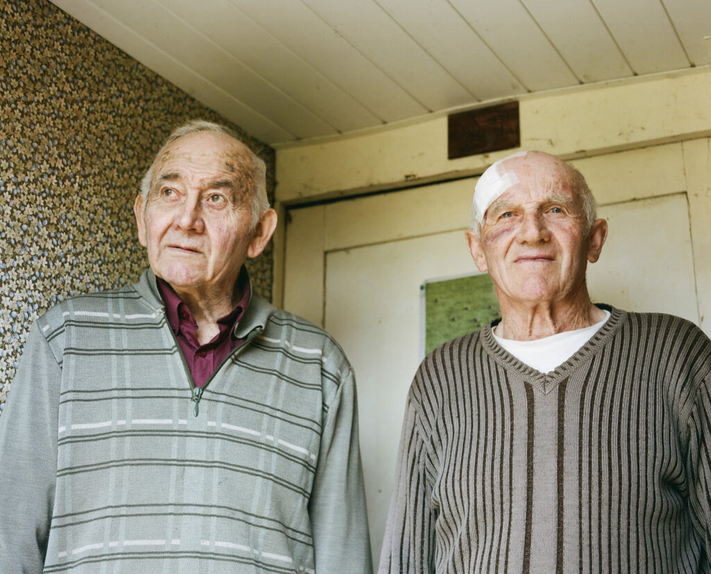Photographie de Zélie Hallosserie / Light Motiv, issue de la série intitulé Jean Marie, représentant un plan poitrine de deux hommes face caméra, à gauche Jacques et à droite son frère Jean-Marie tous deux regardant au loin derrière la caméra, dans l'intention de capturer les moments de vie de Jean Marie.