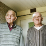 Photographie de Zélie Hallosserie / Light Motiv, issue de la série intitulé Jean Marie, représentant un plan poitrine de deux hommes face caméra, à gauche Jacques et à droite son frère Jean-Marie tous deux regardant au loin derrière la caméra, dans l'intention de capturer les moments de vie de Jean Marie.