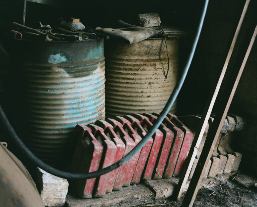 Photographie de Zélie Hallosserie / Light Motiv, issue de la série intitulé Jean Marie, représentant un plan rapproché d'un ensemble de bidons et autres dans ce qui ressemble à un atelier/entrepôt, dans l'intention de capturer les moments de vie de Jean Marie.